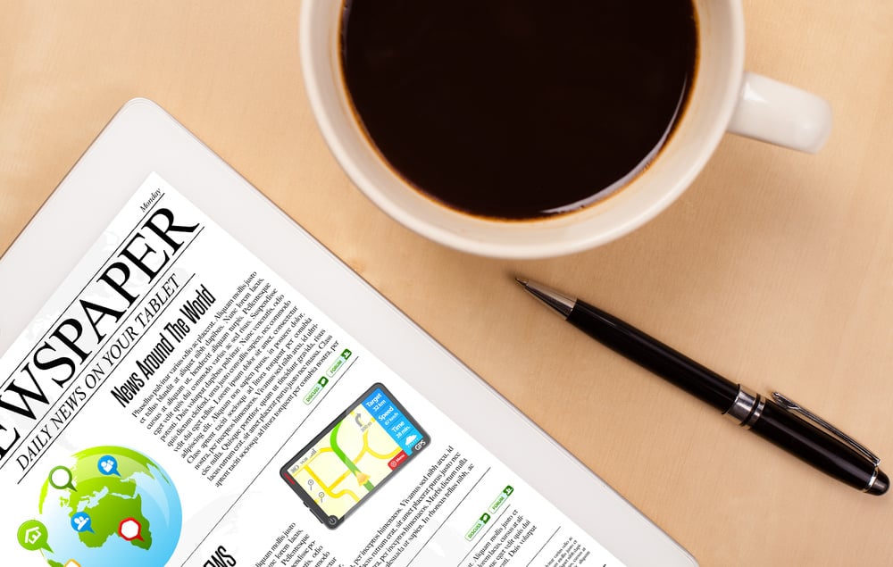 Workplace with tablet pc showing news and a cup of coffee on a wooden work table close-up